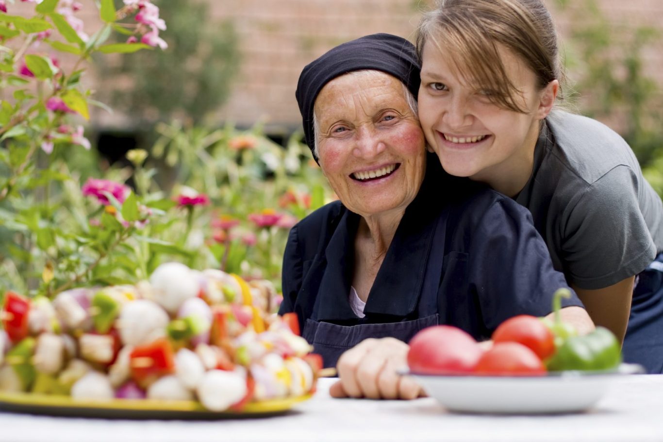Mature woman with a young woman Two women smiling in a garden, with a platter of fresh vegetables in front of them.